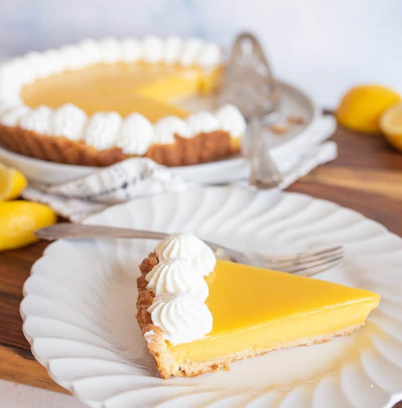 lemon tart on a white plate served from the whole pie