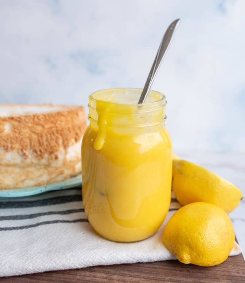 bright yellow lemon curd dripping out of a mason jar with fresh lemons around