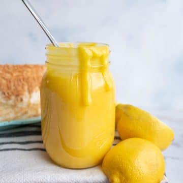 bright yellow lemon curd dripping out of a mason jar with fresh lemons around