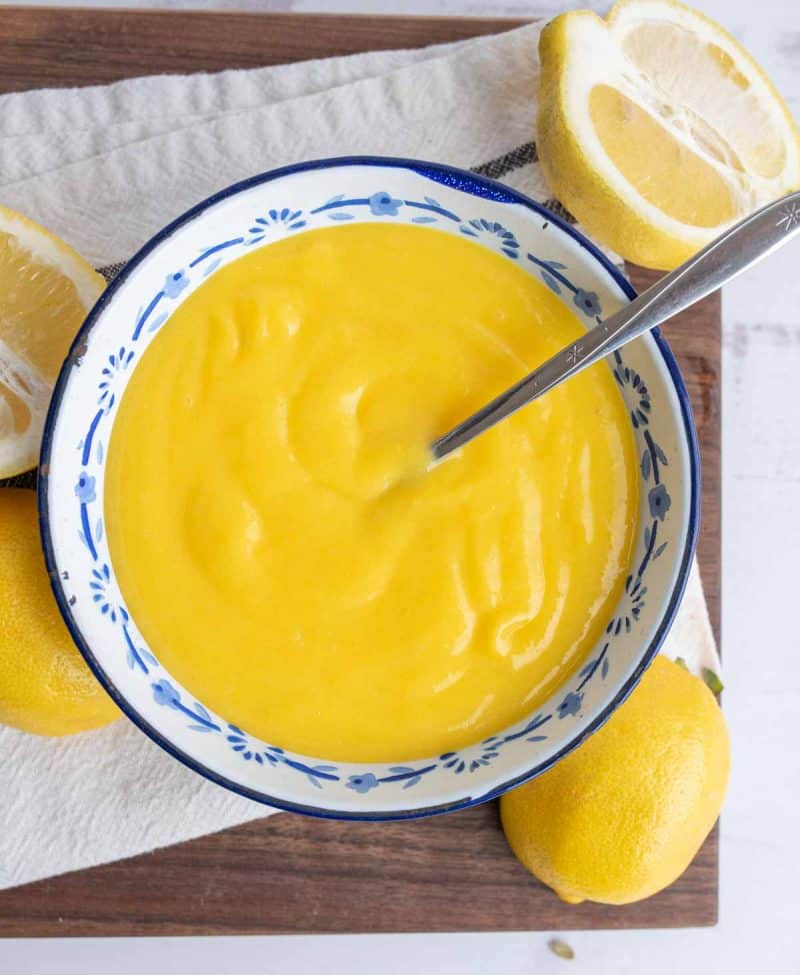 top view of bright yellow lemon curd in a bowl with fresh lemons around