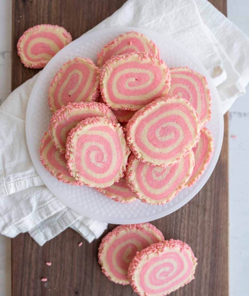 top view of a plate stacked with pink and white pinwheel cookies with a swirl design and pink sprinkles on the edges