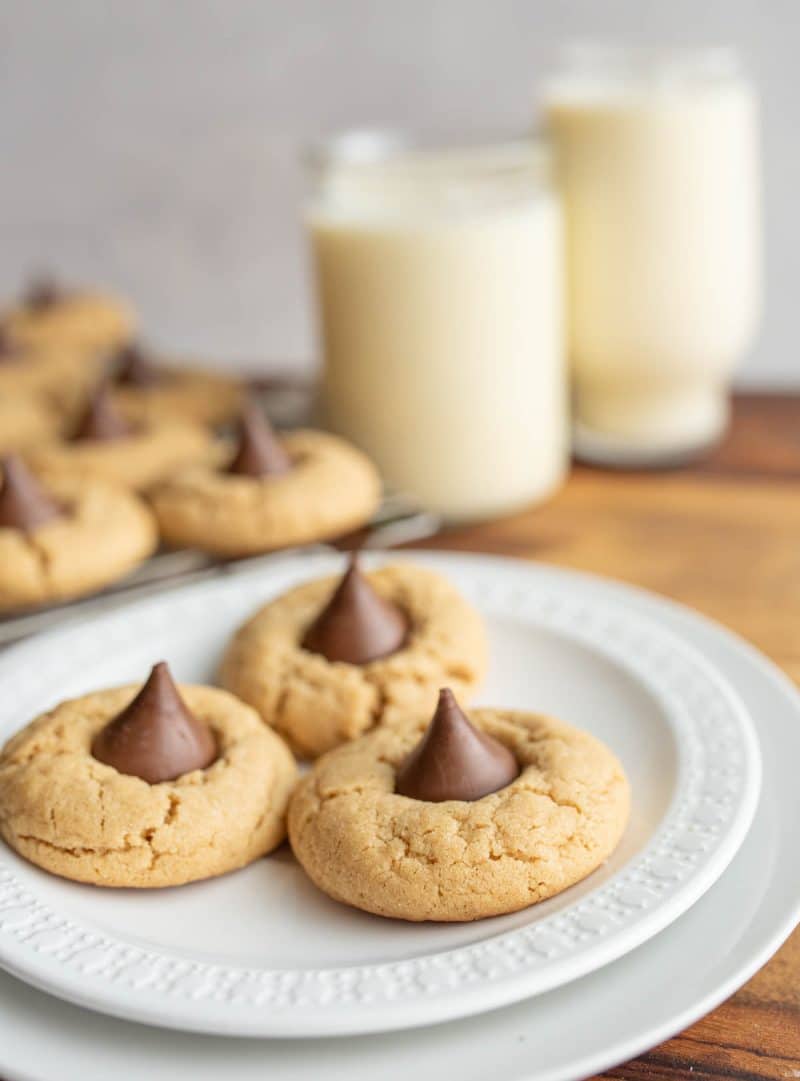 3 hershey kiss cookies on a plate with milk in the background.