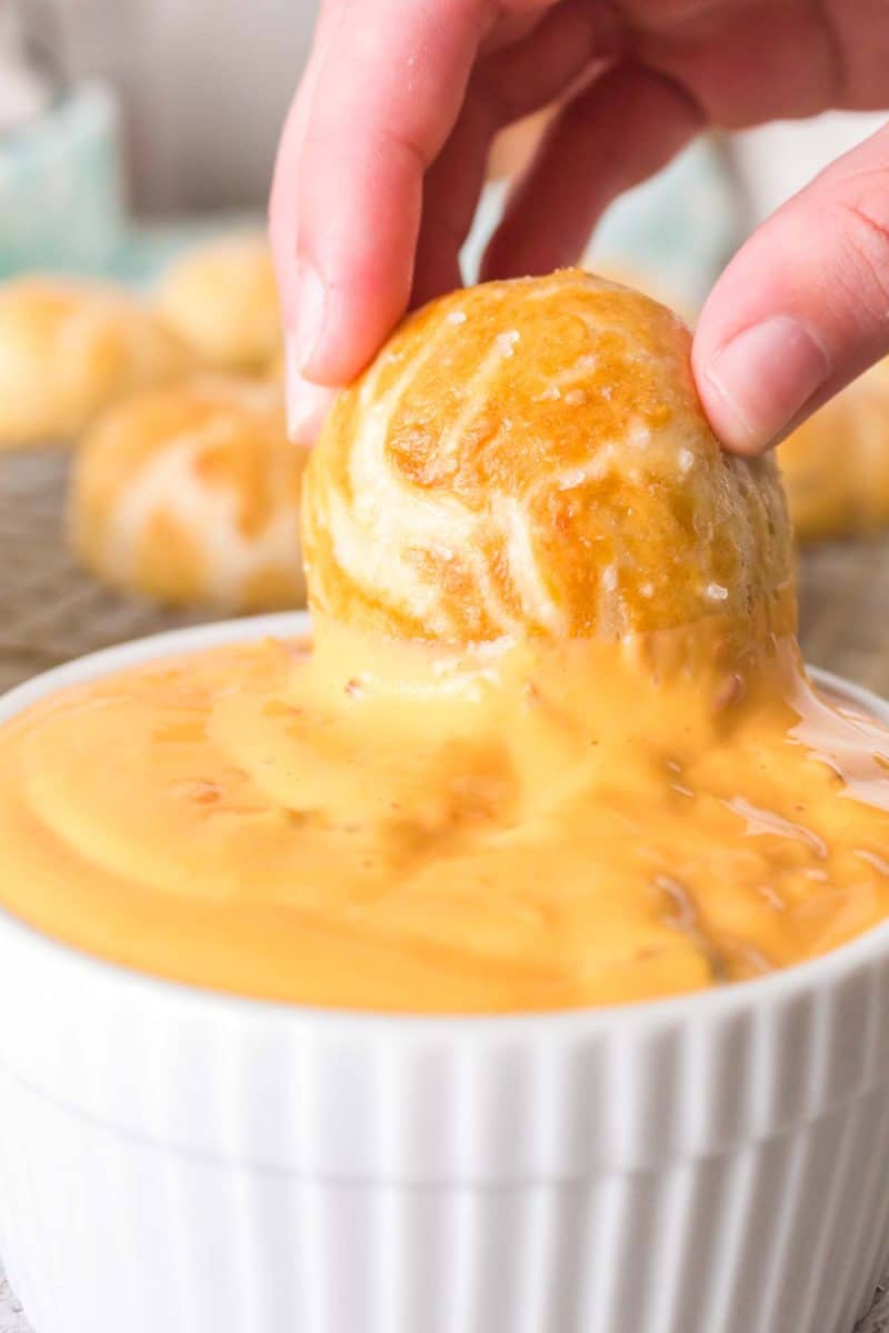 Pretzel bite being dipped into a cheese sauce.