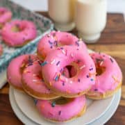 baked donuts stacked on a plate with pink icing and sprinkles