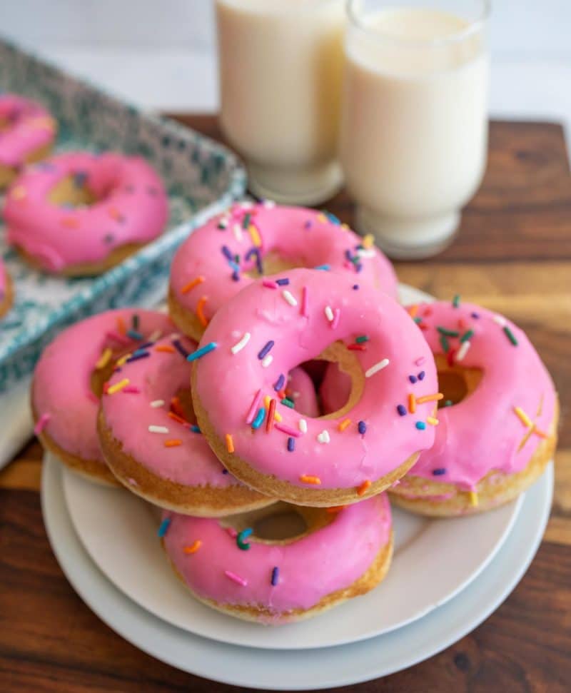 baked donuts stacked on a plate with pink icing and sprinkles