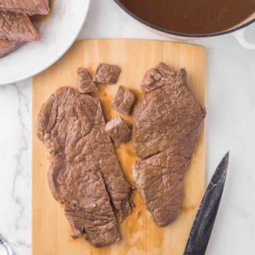 cutting the round-steak on a cutting board with a dutch pot of gravy next to it