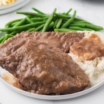 steak with brown gravy next to mashed potatoes green beans on a white plate