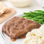 side view of plate of steak with brown gravy mashed potatoes green beans and bread on the side