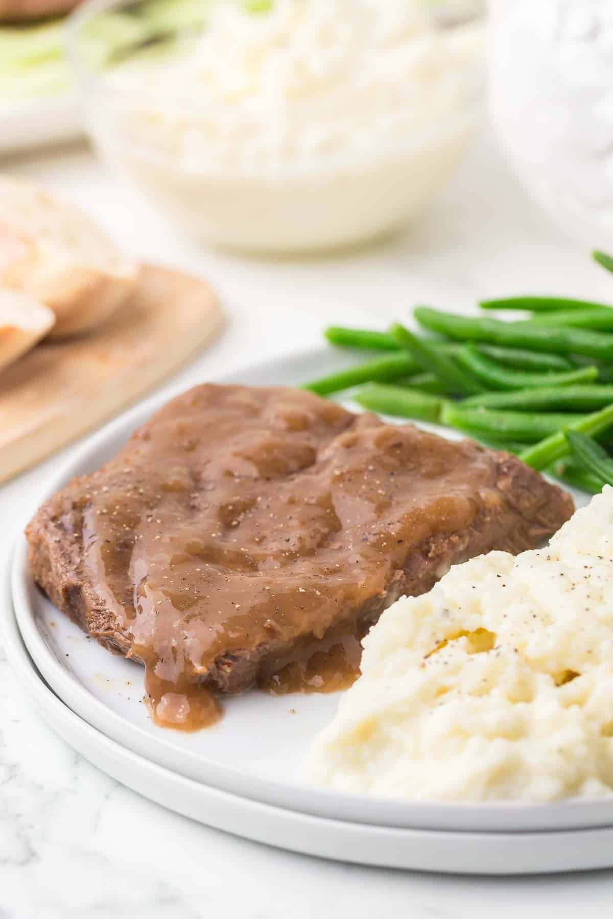 side view of plate of steak with brown gravy mashed potatoes green beans and bread on the side