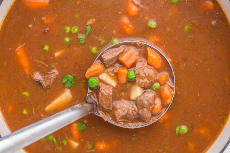 close up of the finished and seasoned round steak beef stew in dutch pot in a ladle