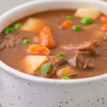 close up of one serving of round steak beef stew in a round white soup bowl