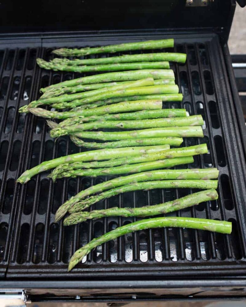 Fresh asparagus spears arranged in a single layer on a black grill, showing how to grill asparagus perfectly outdoors.