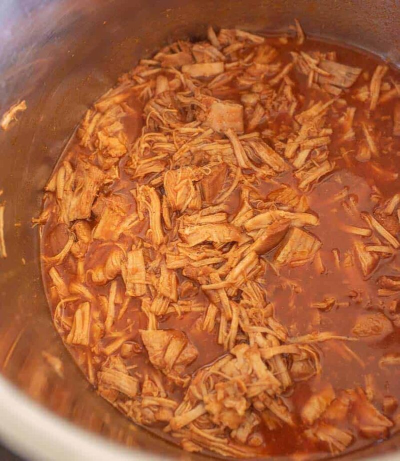 Instant pot pulled pork tenderloin simmers in a rich reddish-brown sauce, filling a large metal pot and suggesting it has been perfectly slow-cooked or braised and is ready to serve.