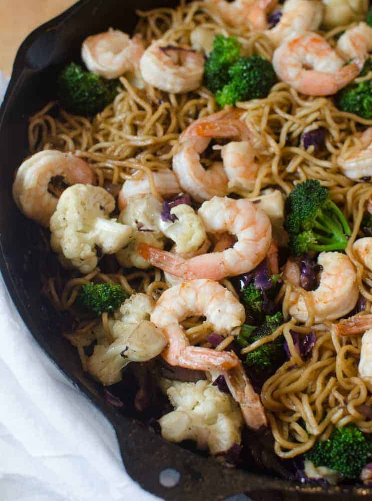 A skillet filled with a vibrant shrimp stir fry recipe—noodles, broccoli, cauliflower, and purple cabbage all cooked together for a colorful meal.