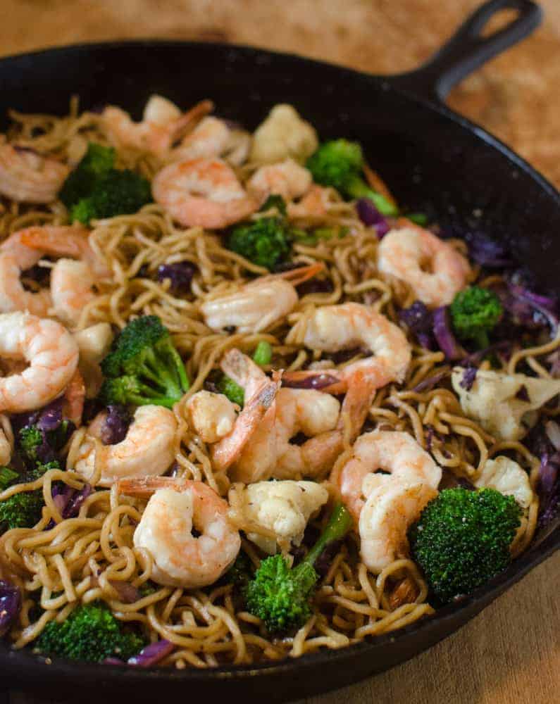 A skillet filled with a delicious shrimp stir fry recipe, featuring noodles, broccoli, cauliflower, and purple cabbage tossed in a savory sauce.