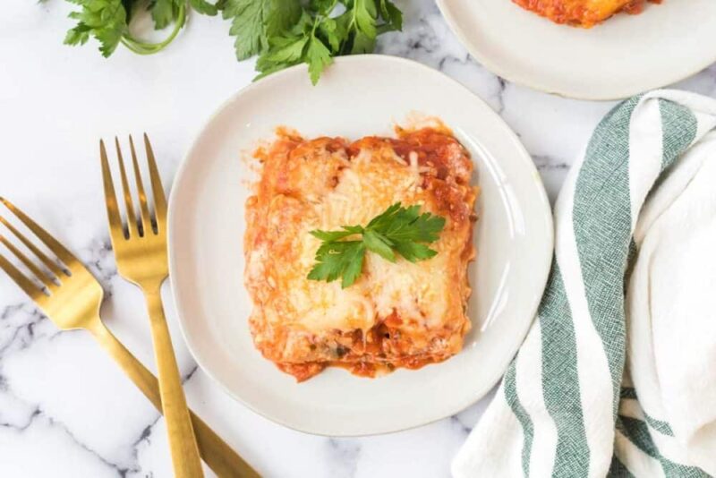 A plate of lasagna with spinach and ricotta rests on a marble surface.