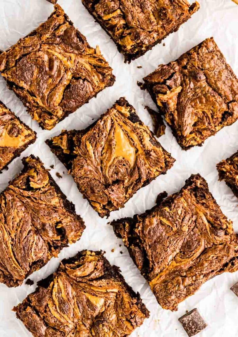 Nine square brownies with a marbled swirl of chocolate and peanut butter on top, arranged on white parchment paper. The brownies have a rich, fudgy texture with visible peanut butter streaks.