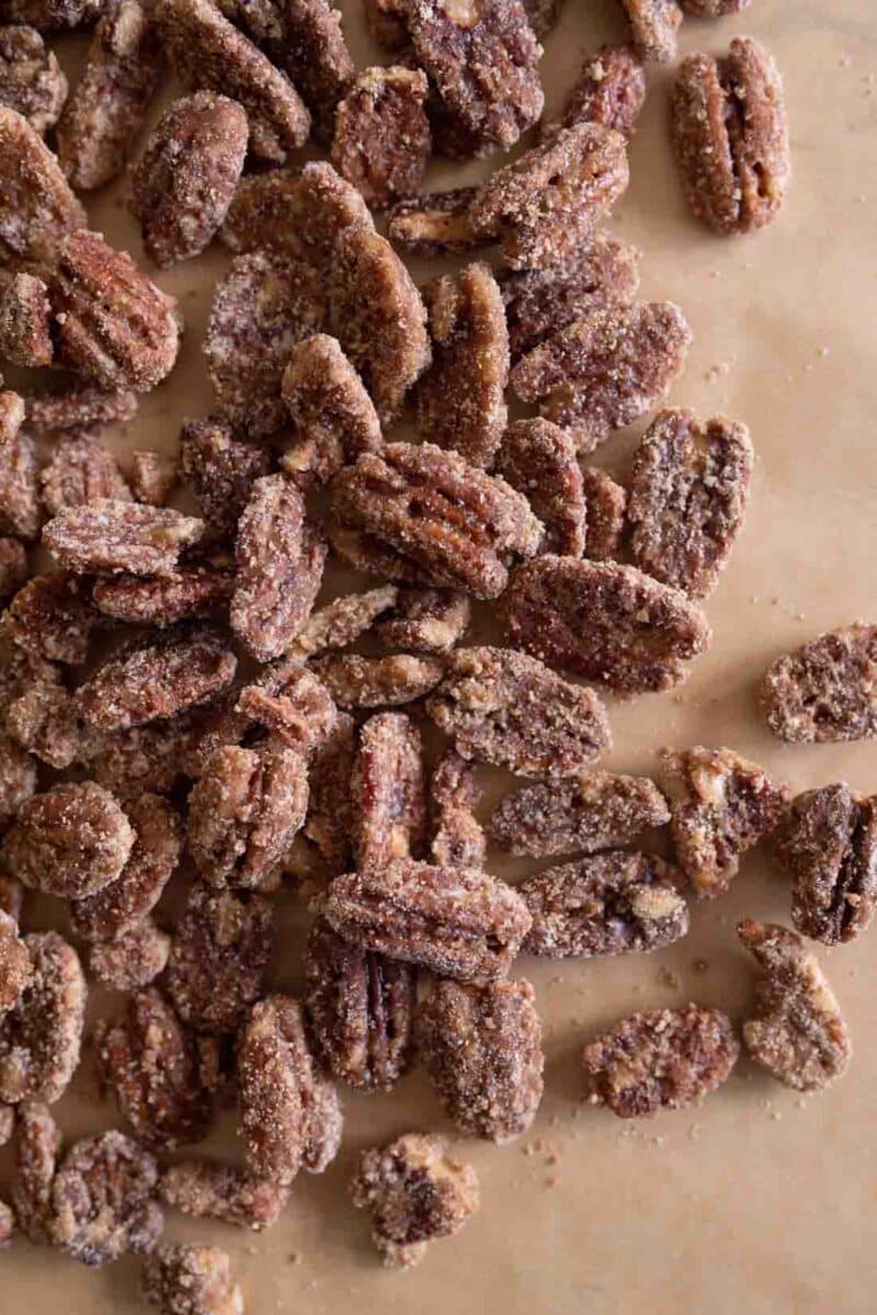 A close-up view of a pile of candied pecans coated in sugar and spices, scattered on a parchment paper surface.