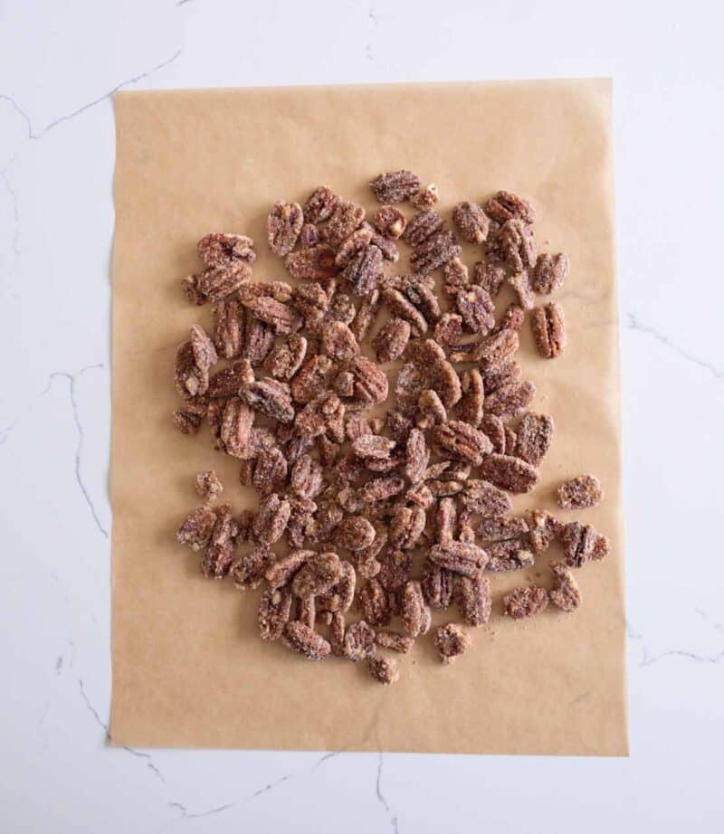 Candied pecans scattered on a sheet of brown parchment paper, placed on a white marble surface.