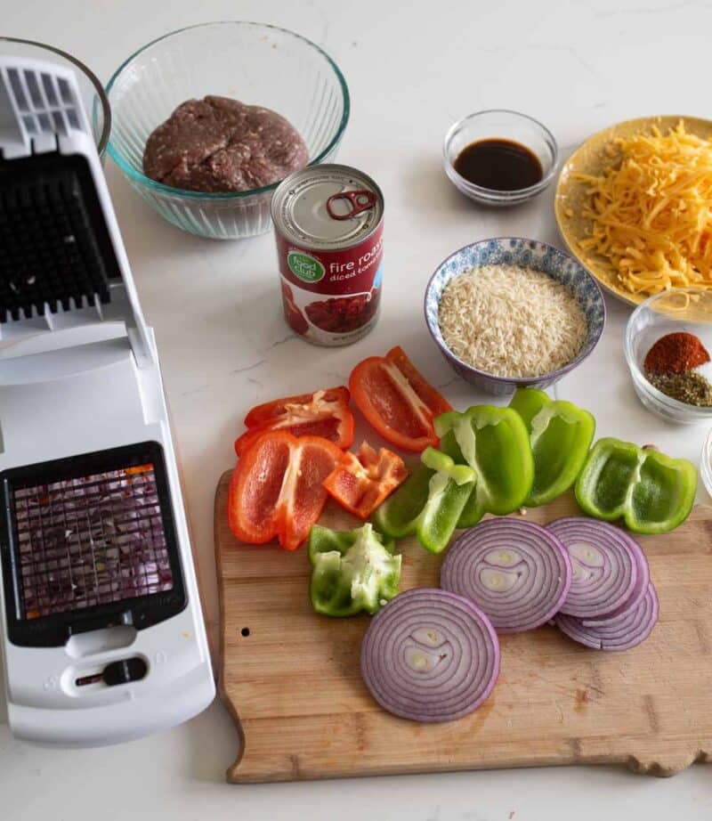 Ingredients for stuffed peppers are prepped: ground meat, diced tomatoes, rice, bell peppers, onions, cheese, and spices. A chopper is on the left.